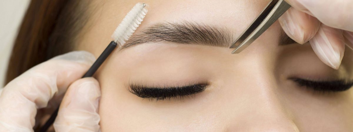 The makeup artist combs her eyebrows with a brush and tweezers. Eyebrow styling. Permanent makeup. Coloring with henna paint.
